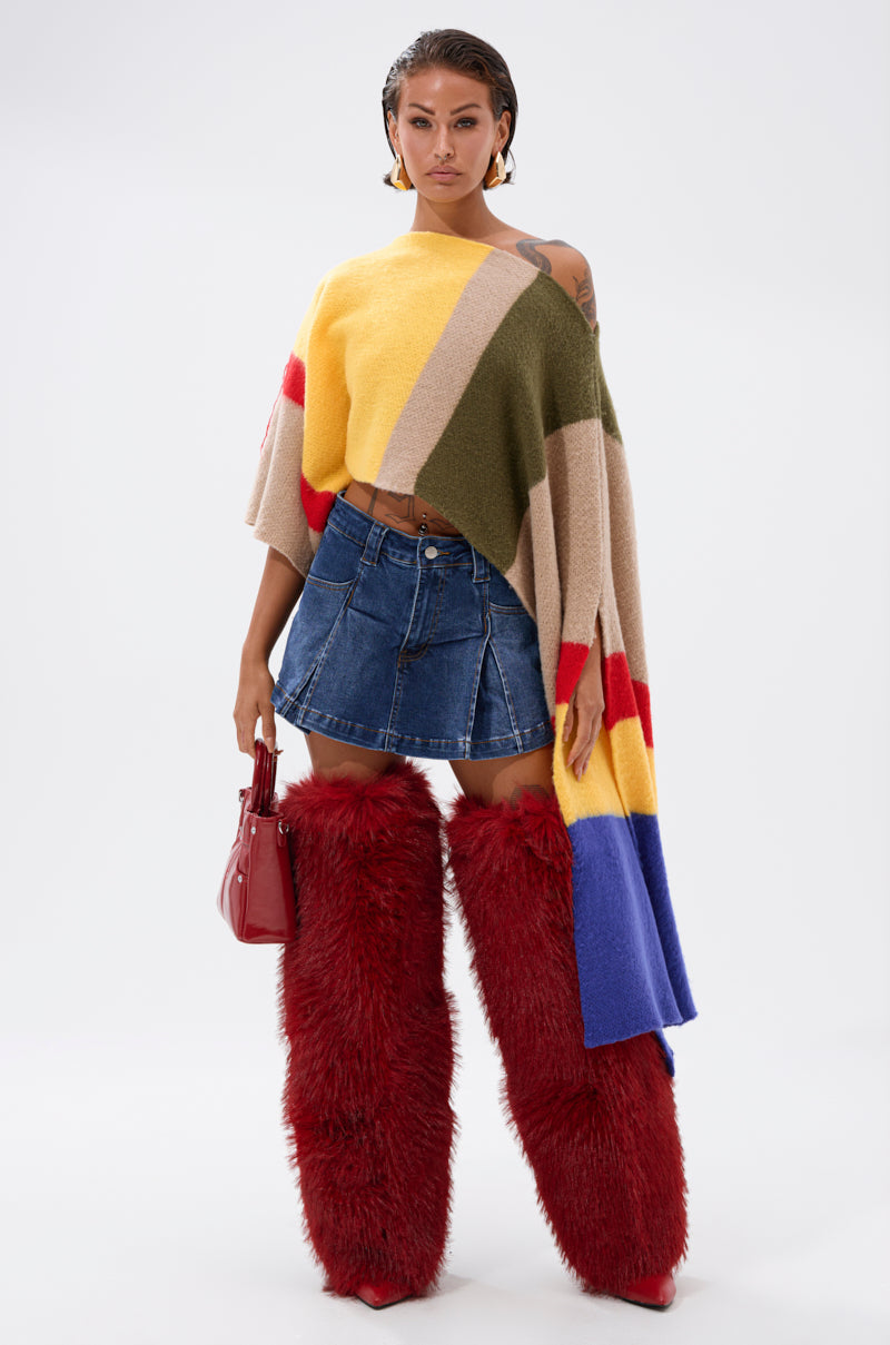 A woman poses in the EASY LOVER CROP ABSTRACT SWEATER, paired with a denim mini skirt and tall red boots. She holds a shiny red handbag, her hair styled wet-look, standing against a plain white backdrop.