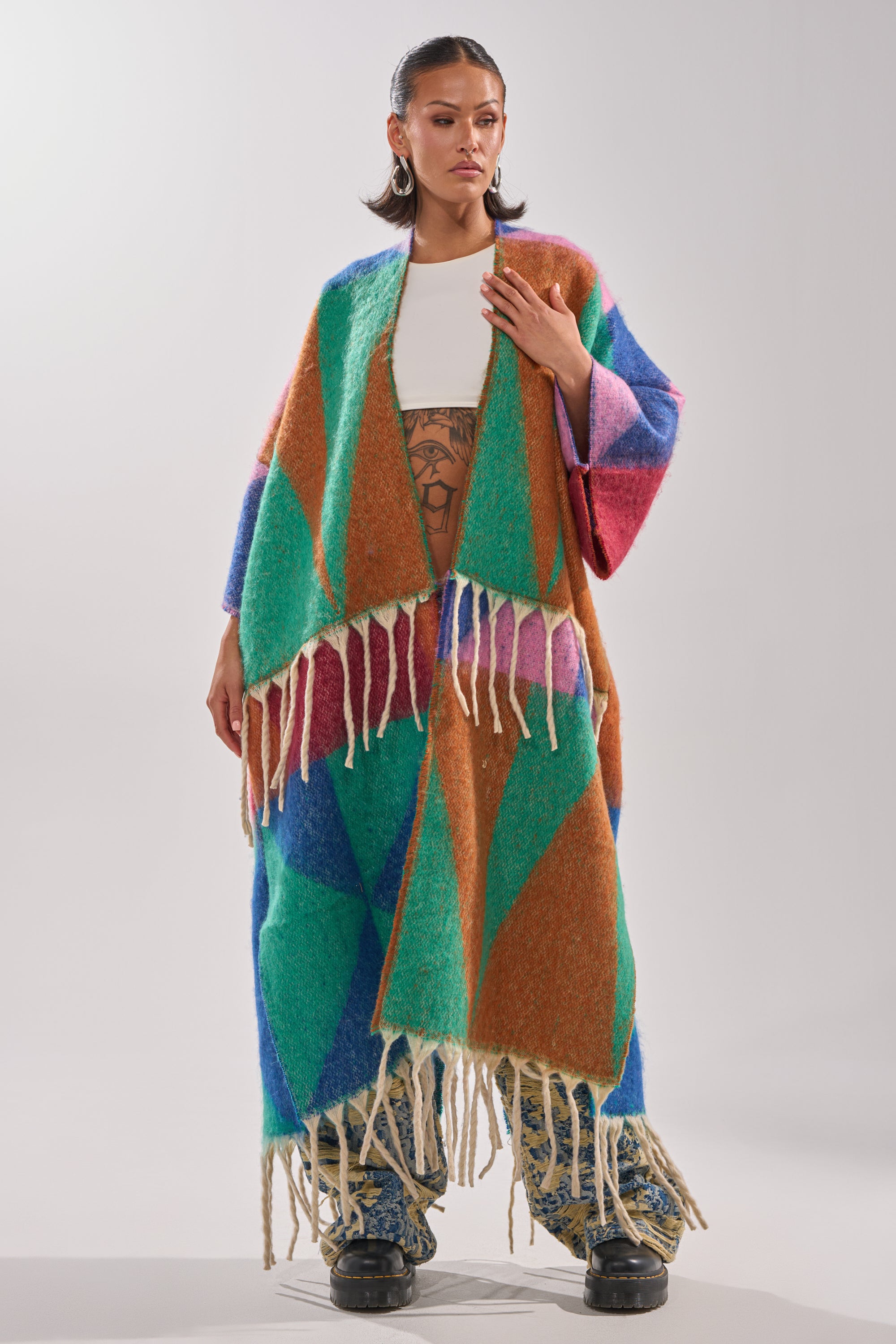 Wearing the FEELING CRAZY OVERSIZED CARDIGAN with a multicolored geometric pattern over a white top and patterned pants, a person stands confidently against a plain background.