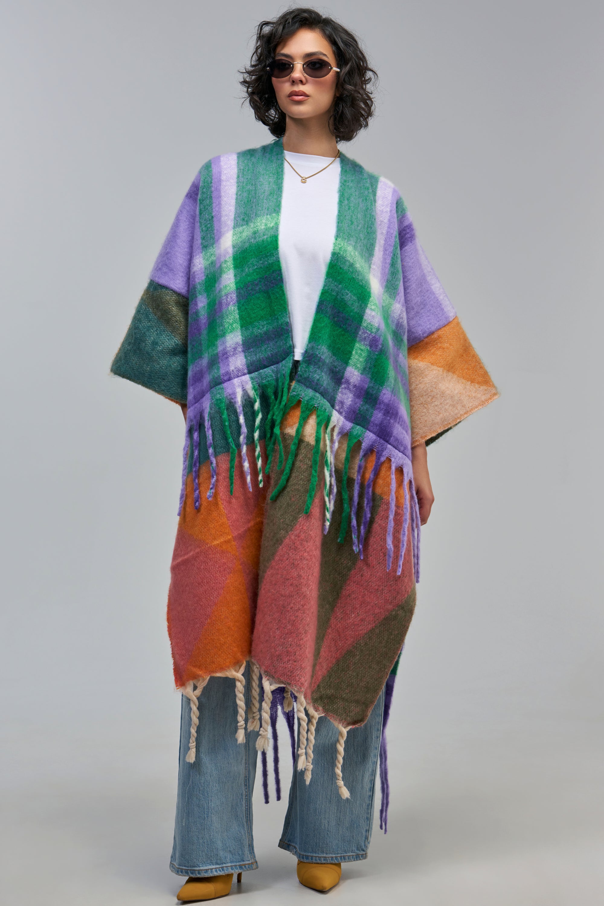A person wears an open-front, fuzzy PASTEL PATCHWORK CARDIGAN with a multicolored pastel patchwork pattern over a white shirt and blue jeans.