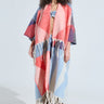 A person with curly hair wearing sunglasses, a BABY PLEASE LOVE CARDIGAN with colorful geometric patterns and fringe tassel detailing, blue jeans, and brown boots stands against a plain background.