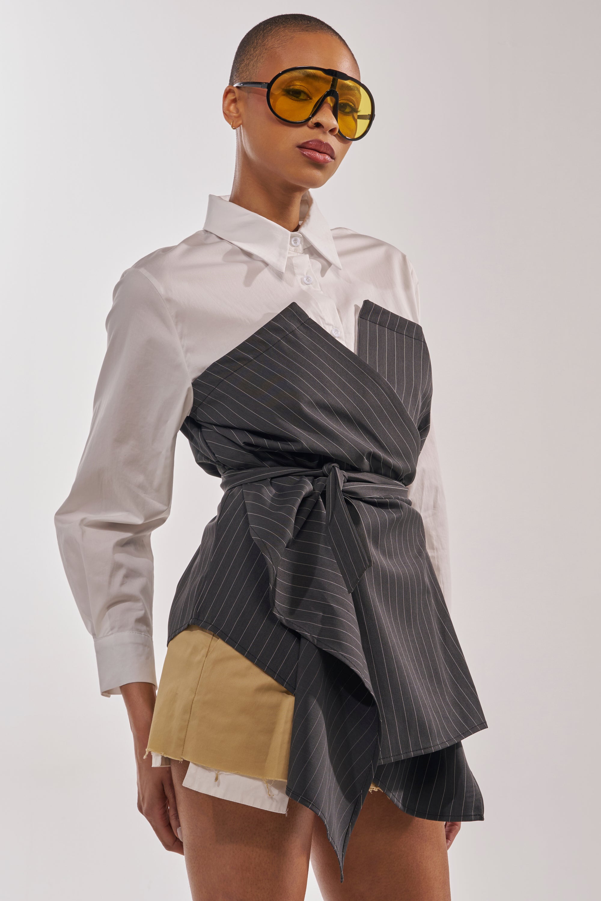 Wearing the BUSINESS ONLY BUTTON DOWN and yellow-tinted sunglasses, a stylish person poses confidently against a plain background, pairing the shirt with tan and white shorts for a chic look. 2