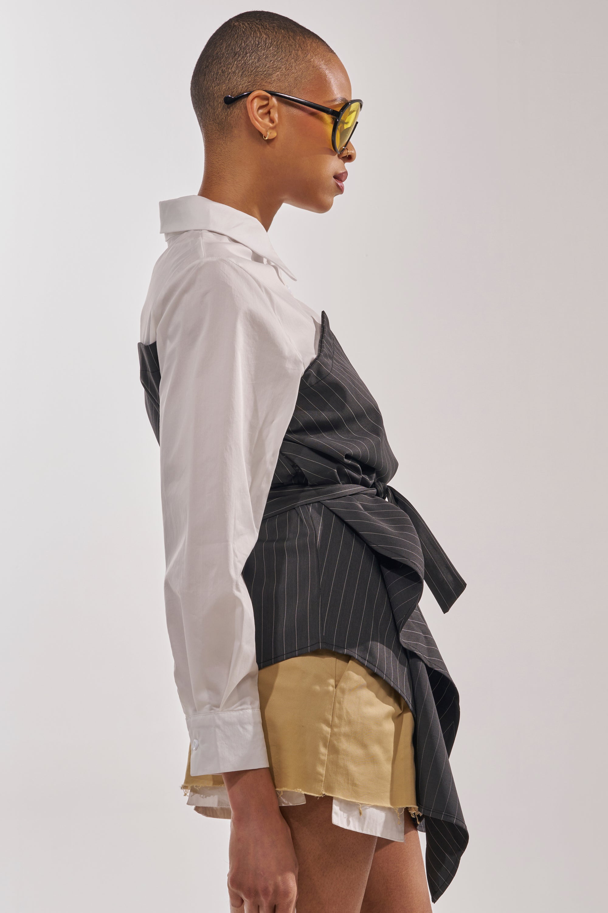 Wearing yellow sunglasses and the BUSINESS ONLY BUTTON DOWN white shirt over tan layered-hem shorts, a person stands in profile against a plain background. 4