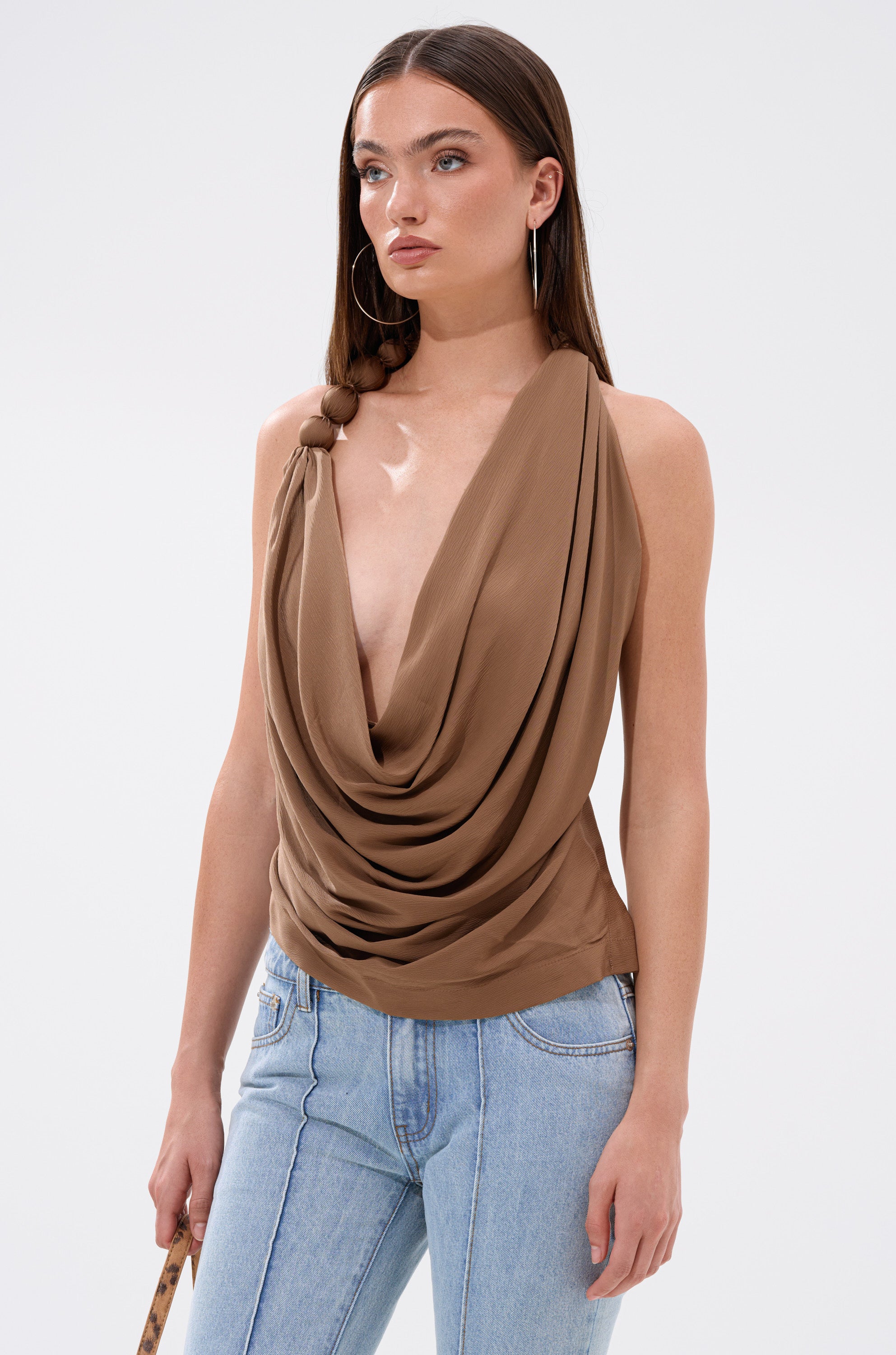 A woman wearing the LEXI SATIN COWL NECK BLOUSE, featuring a brown satin finish and a halter-style neckline.