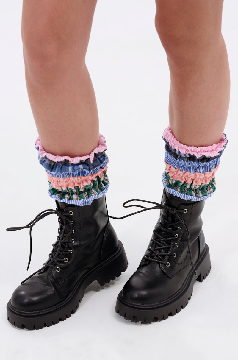 Close-up of a person's lower legs wearing the AZALEA WANG LUBNA BLACK FABRIC DETAIL BOOTIE with chunky rubber soles and colorful ruched leg warmers in pink, blue, green, and white, standing on a white background.