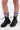 Close-up of a person's lower legs wearing the AZALEA WANG LUBNA BLACK FABRIC DETAIL BOOTIE with chunky rubber soles and colorful ruched leg warmers in pink, blue, green, and white, standing on a white background.