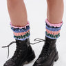 Close-up of a person's lower legs wearing the AZALEA WANG LUBNA BLACK FABRIC DETAIL BOOTIE with chunky rubber soles and colorful ruched leg warmers in pink, blue, green, and white, standing on a white background.