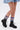 A person stands against a plain white background wearing a light denim skirt, colorful ruched leg warmers in pink, purple, green, and blue, and AZALEA WANG LUBNA BLACK FABRIC DETAIL BOOTIE combat boots with chunky rubber soles.