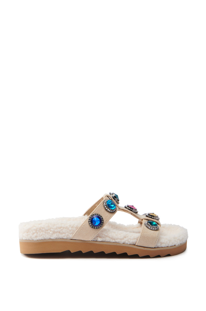 Side view of the AZALEA WANG LUCIENA beige sherpa sandal featuring a fluffy sole, two suede foot bands with colorful rhinestones, and a wavy brown rubber sole.