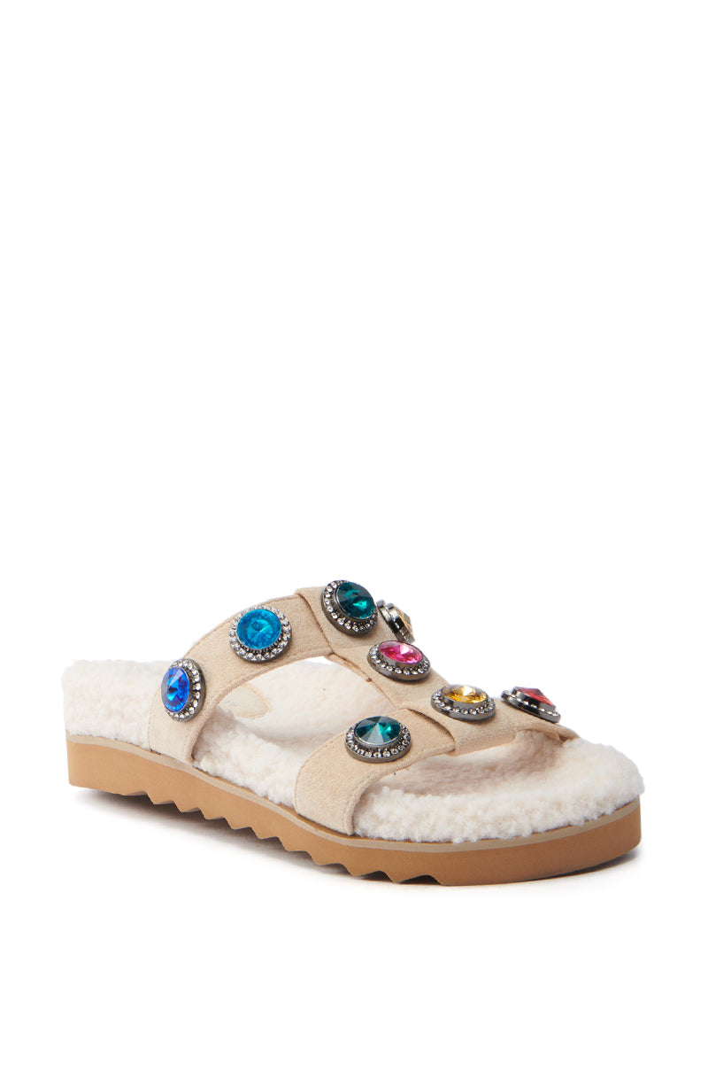 The AZALEA WANG LUCIENA BEIGE RHINESTONE AND SHERPA SANDAL features tan suede foot bands with multicolored gemstones, a thick zigzag-patterned sole, and a fluffy white fleece-textured footbed.