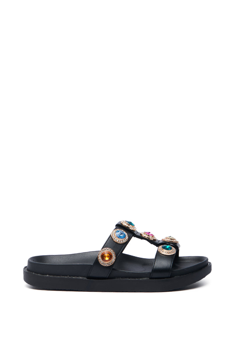 The AZALEA WANG LUCIENA BLACK RHINESTONE SANDAL features two straps with vibrant gem detailing. Crafted from vegan leather, it has a casual design with a flat sole, making it ideal for relaxed occasions.
