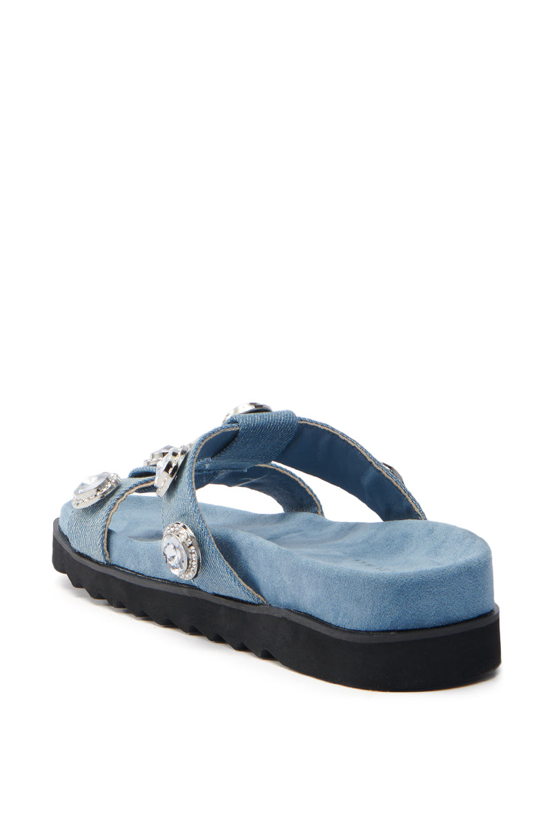 The AZALEA WANG LUCINEA DENIM RHINESTONE SANDAL is a blue open-toed sandal with a thick black sole, multiple silver buckles, and cross-over straps. It features a textured footbed and sparkles beautifully from the side view.