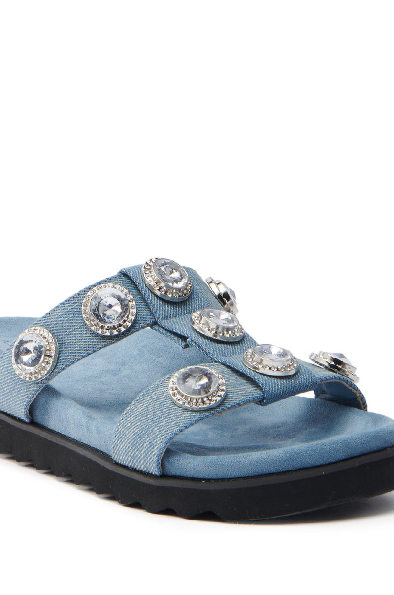 The AZALEA WANG LUCINEA DENIM RHINESTONE SANDAL is shown in blue denim with a black sole and wide straps featuring large round silver and crystal embellishments, offering a decorative and stylish look against the plain white background.