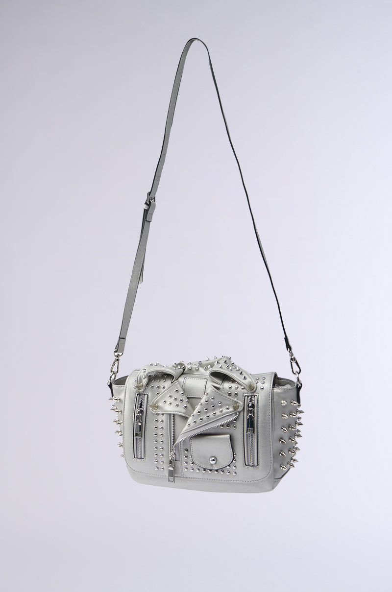 The MOTO OF YOUR DREAMS PURSE is a stylish gray faux leather purse with an adjustable strap, accented by metal studs. It features a front pocket with a zipper and buckle detail, resembling a moto jacket, set against a simple light gray gradient background.