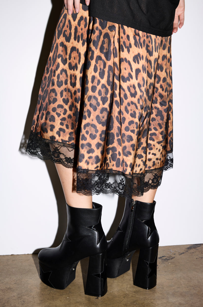 A person wearing a leopard print skirt with lace trim and AZALEA WANG LUKYIE Black Star Detail Platform Booties stands on a concrete floor against a white background.