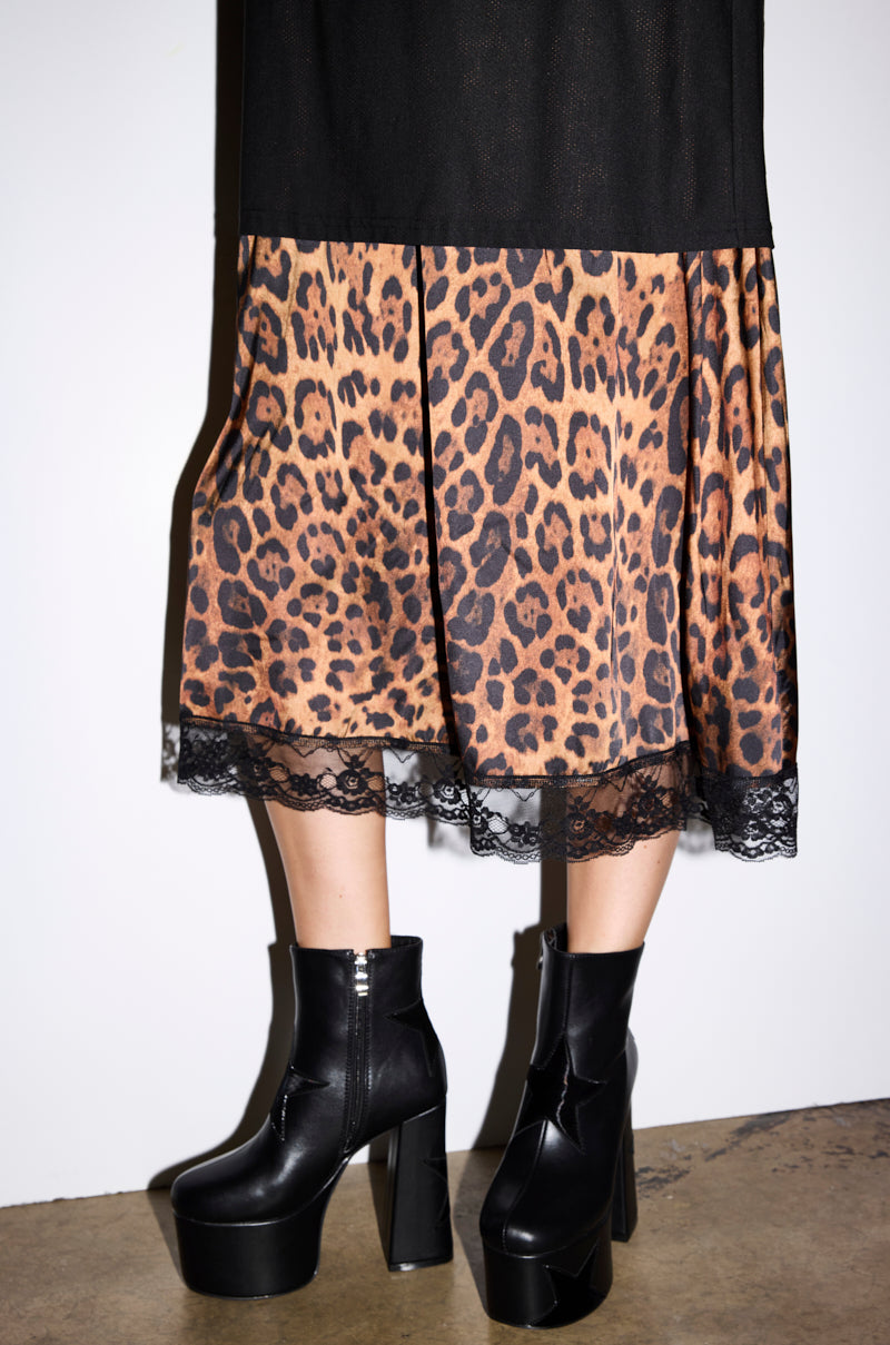 A person in a black leopard print skirt with lace trim stands on concrete, paired with the AZALEA WANG LUKYIE Black Star Detail Platform Bootie featuring a chunky heel.