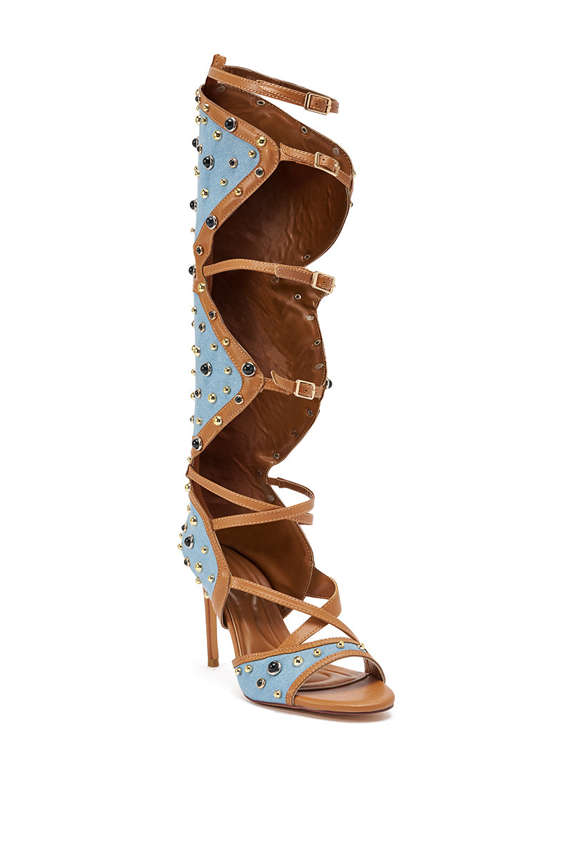 The AKIRA GOLD LULANA DENIM METAL STUDDED GLADIATOR STILETTO SANDAL features light blue denim panels, brown leather trim, gold studs, and multiple straps with buckles running up to just below the knee. 6