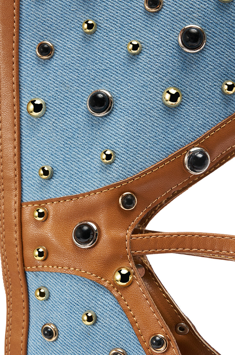 Close-up of the AKIRA GOLD LULANA DENIM METAL STUDDED GLADIATOR STILETTO SANDAL—blue denim and tan leather detailed with gold and black metal studs, gladiator-inspired design, intricate texture, and precise stitching. 8