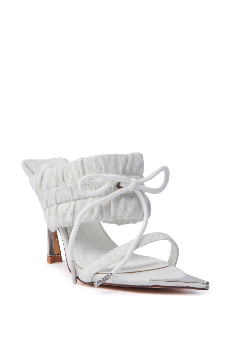 The AZALEA WANG LUNETTE GREY SANDAL is a white stiletto heel with silver accents, featuring a puffy, padded strap and an open pointed toe with a bow. Its metallic, angular heel contrasts beautifully with the soft-textured upper material.