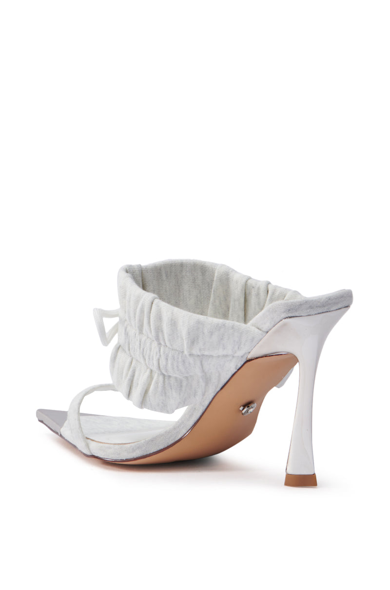 The AZALEA WANG LUNETTE GREY SANDAL is showcased in a minimalist style, highlighting its stiletto heel from the back. It features a ruched fabric strap, open pointed toe, lightly cushioned footbed, and tan sole on a white backdrop.