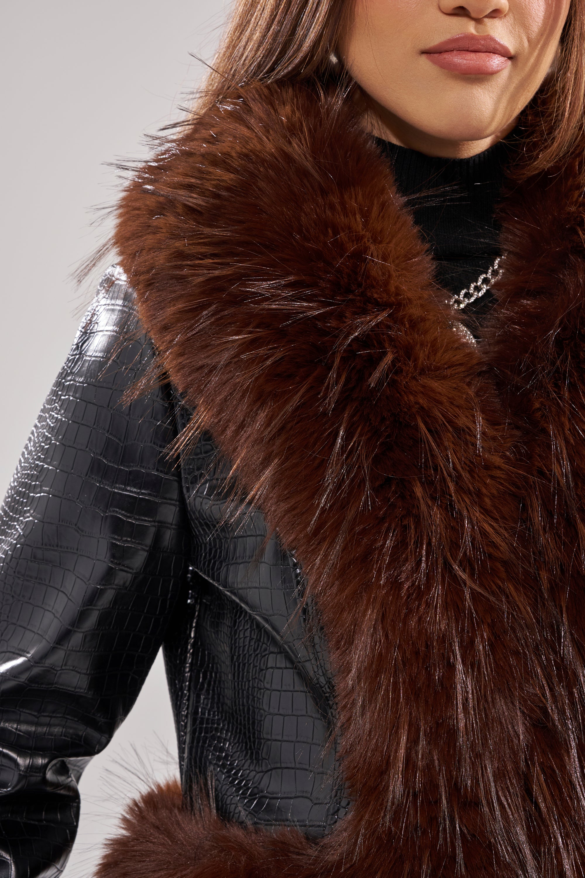 A woman wears the LUNNA FUR TRIM MOTO IN BLACK CROC, featuring a large, fluffy brown fur collar over a black turtleneck, shown from shoulders to mid-chest.