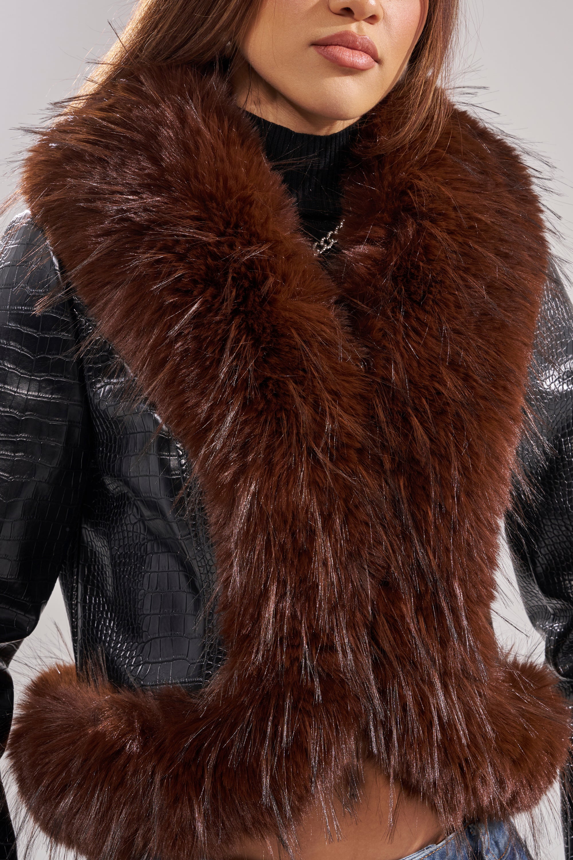 A woman wears the LUNNA FUR TRIM MOTO IN BLACK CROC, featuring bold croc texture and plush brown faux fur trim draped over her shoulders, exuding a stylish edge with her hands on her hips and face partially visible.