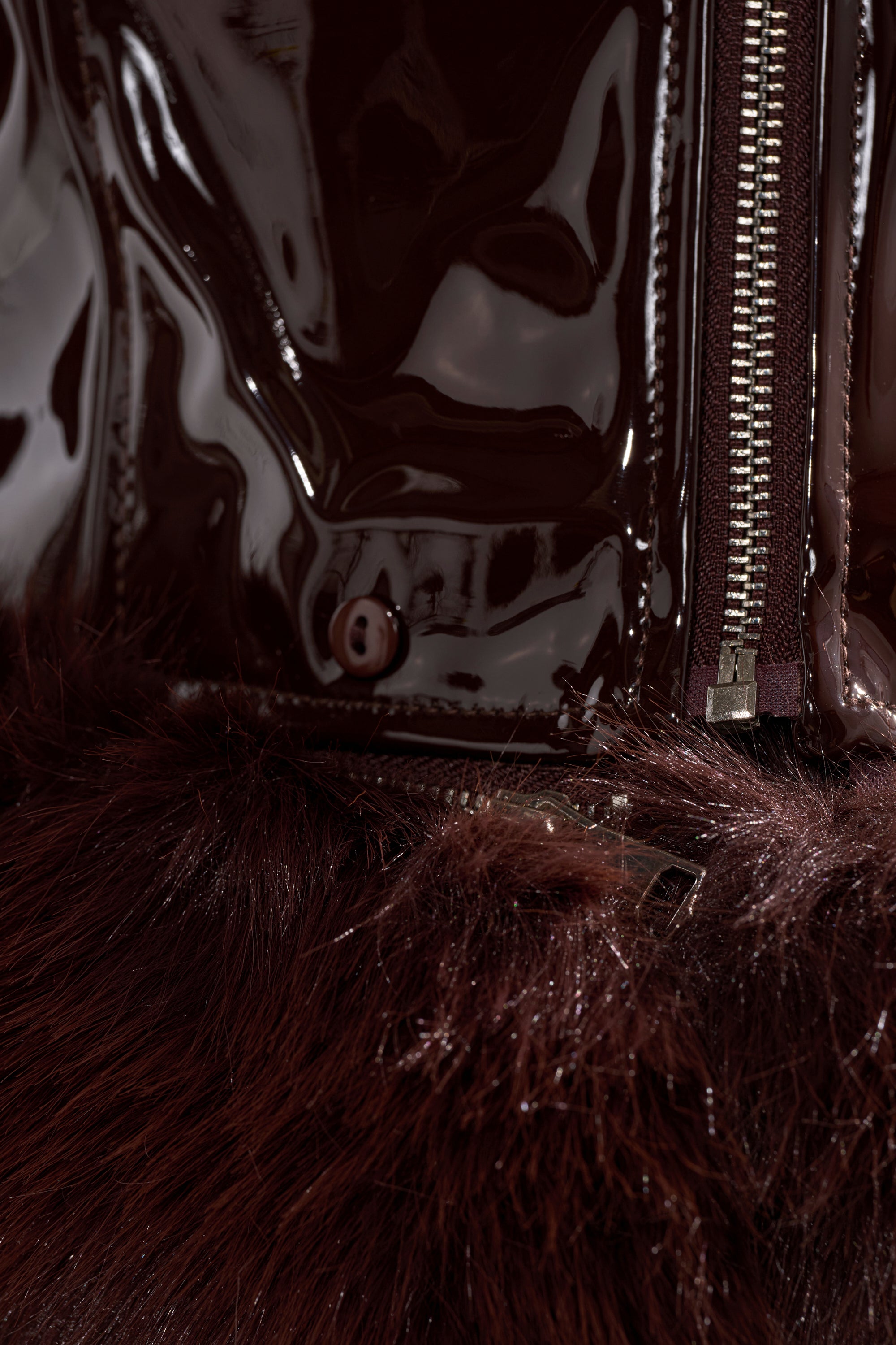Close-up of the LUNNA FUR TRIM MOTO IN PATENT, a glossy dark burgundy faux leather jacket with a shiny metal zipper, buttons, and matching dark burgundy faux fur trim.