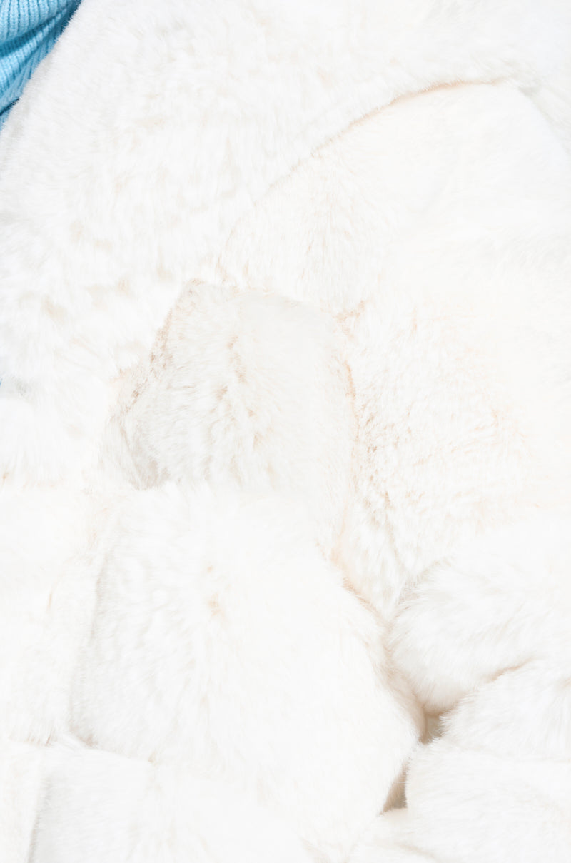A close-up of the soft, fluffy white fabric showcases a cozy texture, complemented by a touch of blue fabric in the upper left corner. This image evokes the warmth and comfort synonymous with the LUXE JENNY HOODED FAUX FUR TRENCH IN WHITE from AKIRA Label, reminiscent of a plush surface or blanket.