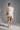 A woman stands in a studio wearing the LUX WAVES MINI SKIRT, a chic high-waist mini skirt, paired with a white lace top featuring an oversized bow, lace gloves, and tall white platform boots. Her hair is sleek and her expression neutral.