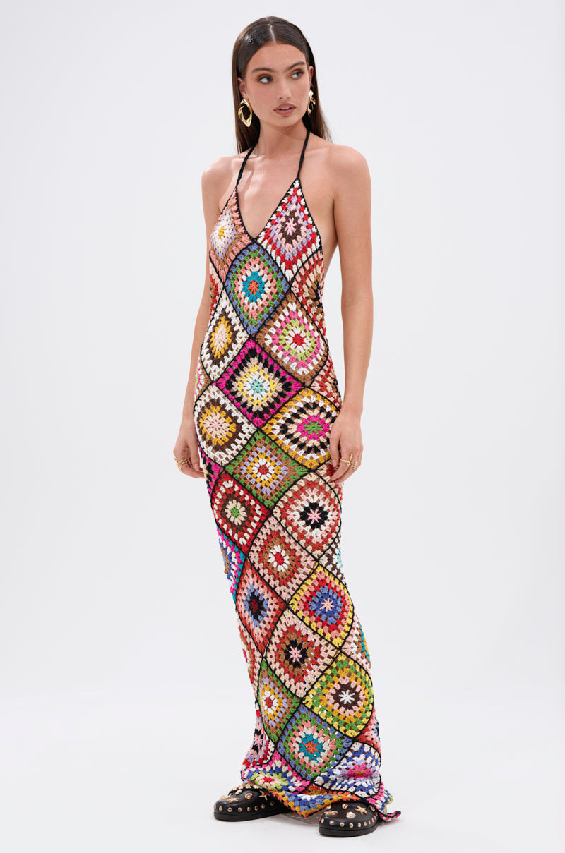 A woman wears the DONT LET ME GO CROCHET MAXI DRESS, featuring vibrant multicolored diamond-patterned granny squares for a beach-ready vibe, styled with black platform sandals, long straight hair, and gold hoop earrings.