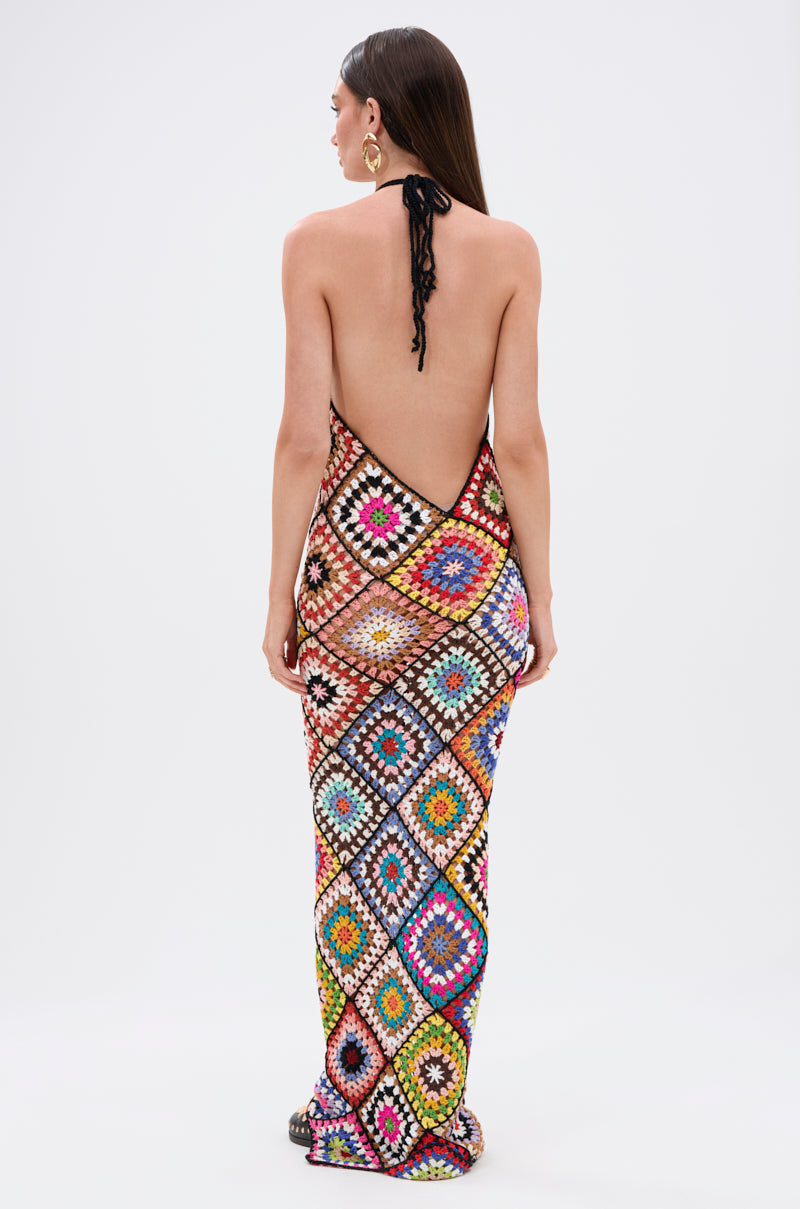 A woman with long brown hair models the DONT LET ME GO CROCHET MAXI DRESS, featuring a vibrant multicolored pattern and open back. She stands facing away against a white background, highlighting her chic, beach-ready style.