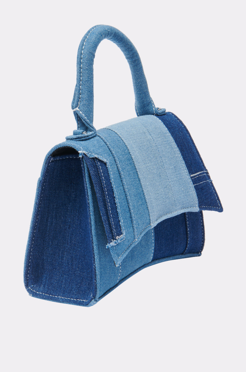 The WESTIE PATCHWORK DENIM PURSE is a small denim bag in blue shades with a top handle, shoulder strap, and flap closure, displayed against a plain light background. 3