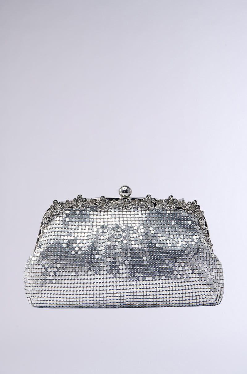 The WALK IT OUT EMBELLISHED CHAINMAIL CLUTCH features a silver design with rhinestone trim and a mesh of shiny metallic beads, complemented by a clasp shaped like a small rounded knob, all set against a gradient light grey background.