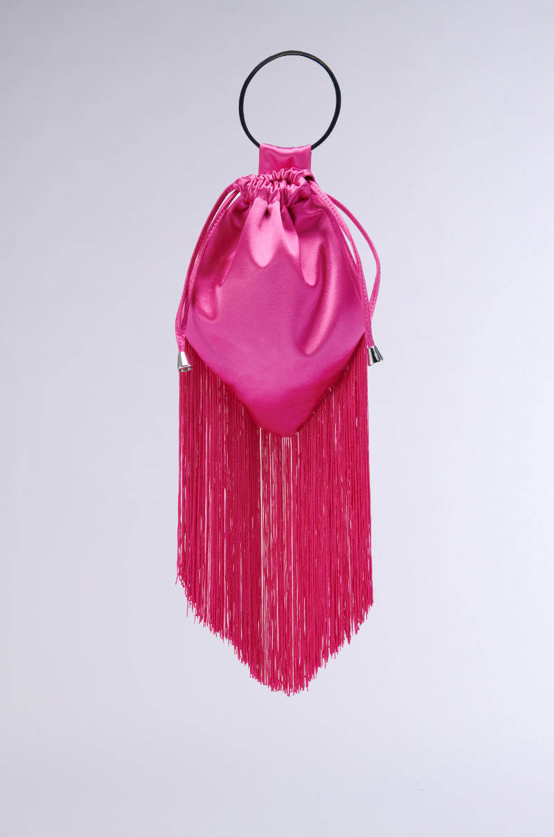 The GNO Satin Fringe Purse is a vibrant pink satin drawstring bag with a distinct upside-down triangular shape. It features long pink fringes hanging from the bottom and a black round handle at the top, exuding a bold, stylish, and contemporary look. The purse also comes with a detachable silver chain link strap for added versatility.