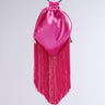 The GNO Satin Fringe Purse is a vibrant pink satin drawstring bag with a distinct upside-down triangular shape. It features long pink fringes hanging from the bottom and a black round handle at the top, exuding a bold, stylish, and contemporary look. The purse also comes with a detachable silver chain link strap for added versatility.