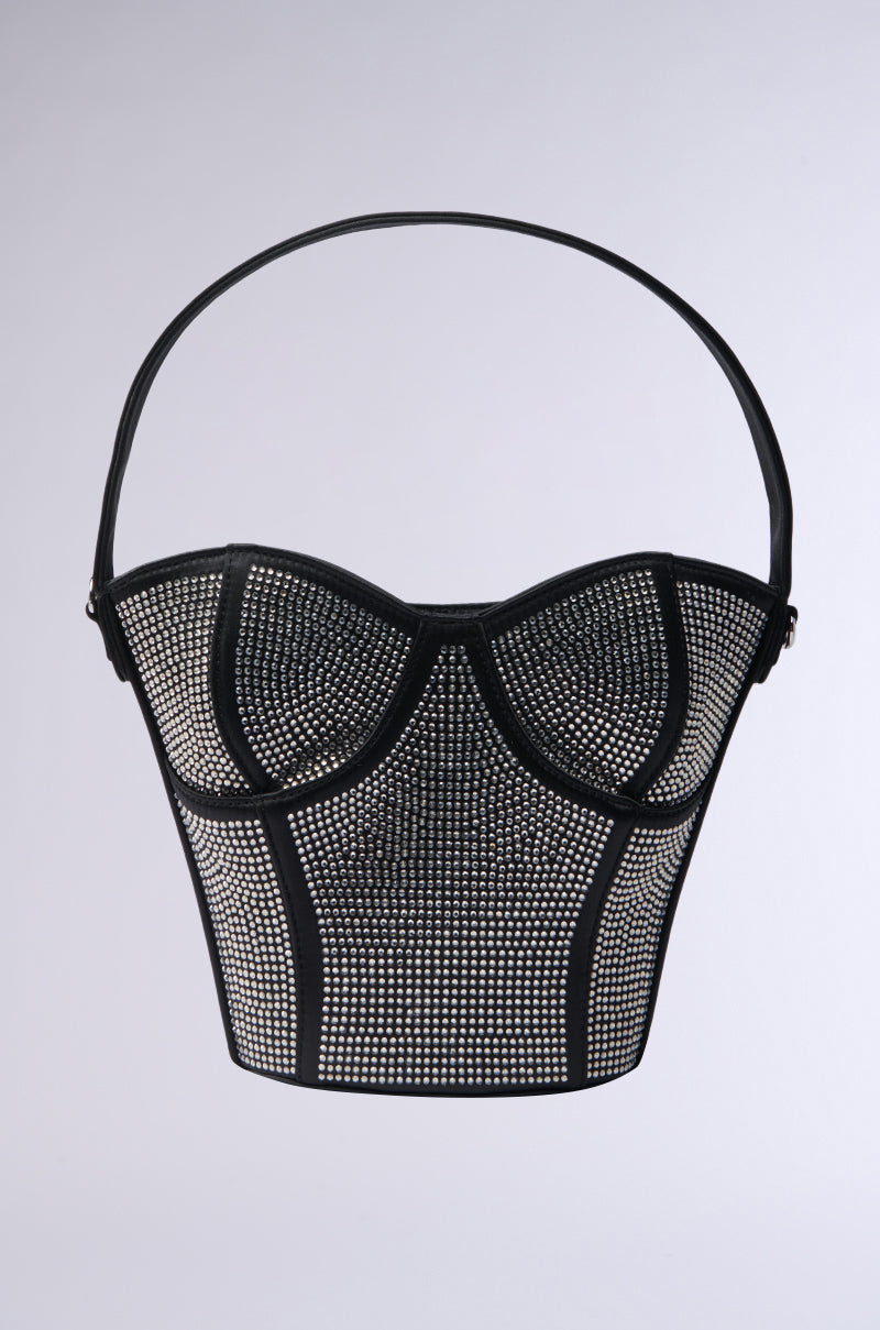 The HOLD MY BUSTIER PURSE is a black bag with silver studs and rhinestone details, shaped like a bodice. It features a single strap handle and is displayed on a plain gray background.