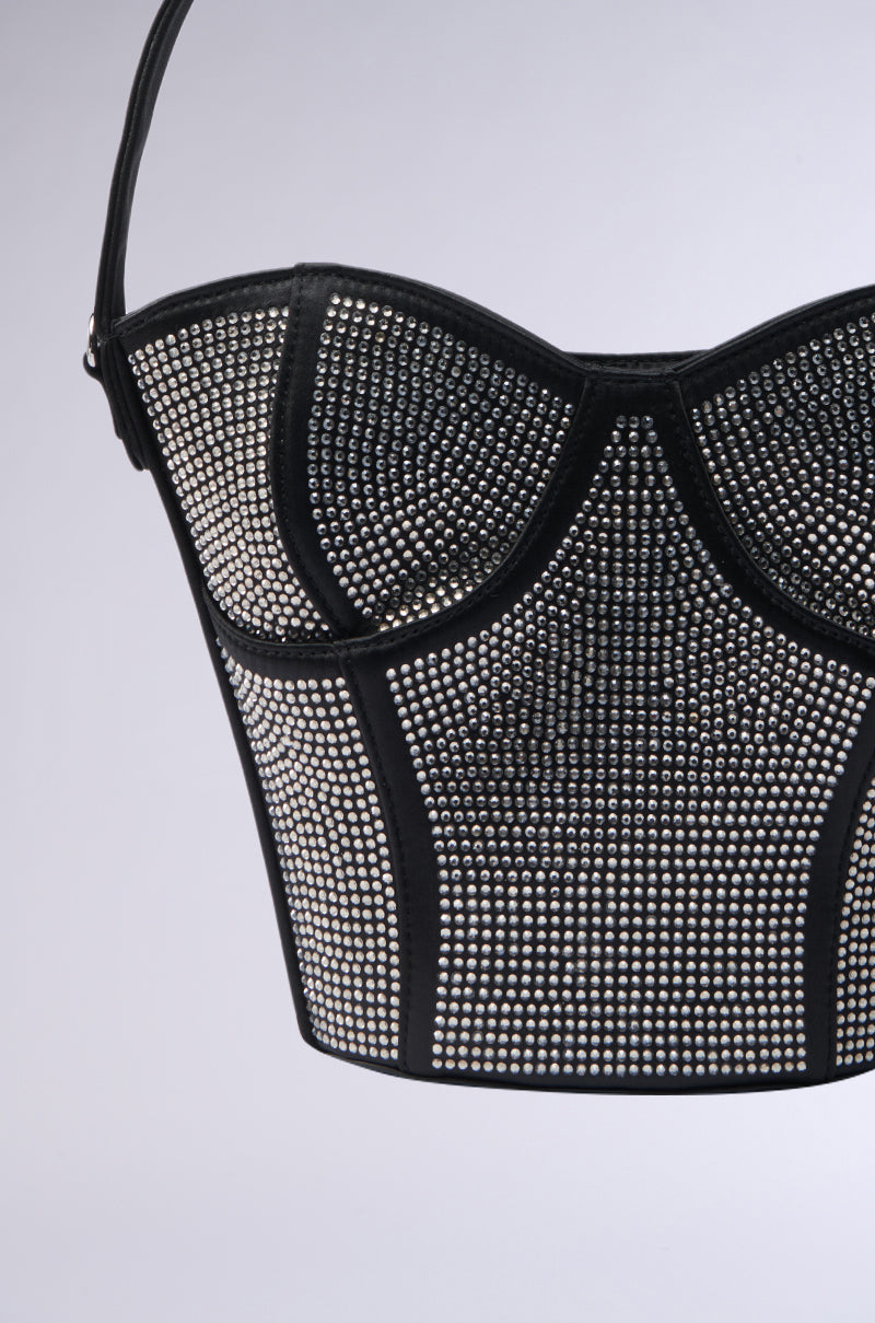 A black corset-style top embellished with small silver studs offers structured cups and vertical panels for a fitted, intricate look. Pair it with the HOLD MY BUSTIER PURSE, a satin handbag, for added elegance. Background: plain light gray.