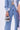 A person in light blue denim jeans and a matching jacket holds the LOVE MY VIBE HAMMERED CHROME PURSE with a textured hammered finish. Only their torso and upper legs are visible; they stand beside someone dressed in pink.