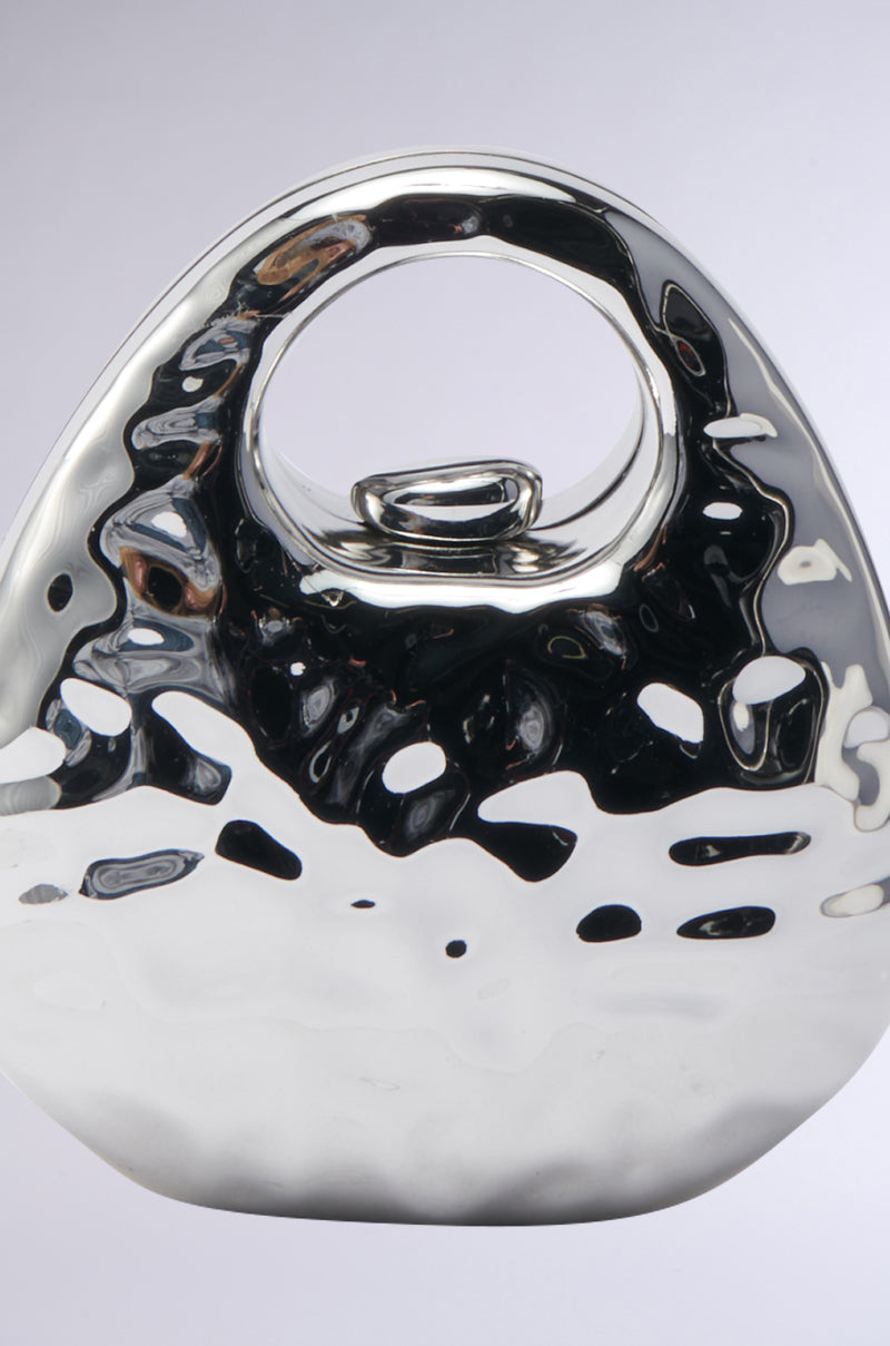 The LOVE MY VIBE HAMMERED CHROME PURSE is a shiny, abstract silver accessory with a rounded shape, a large oval opening near the top, and a textured hammered finish that reflects light with smooth, undulating surfaces. 4