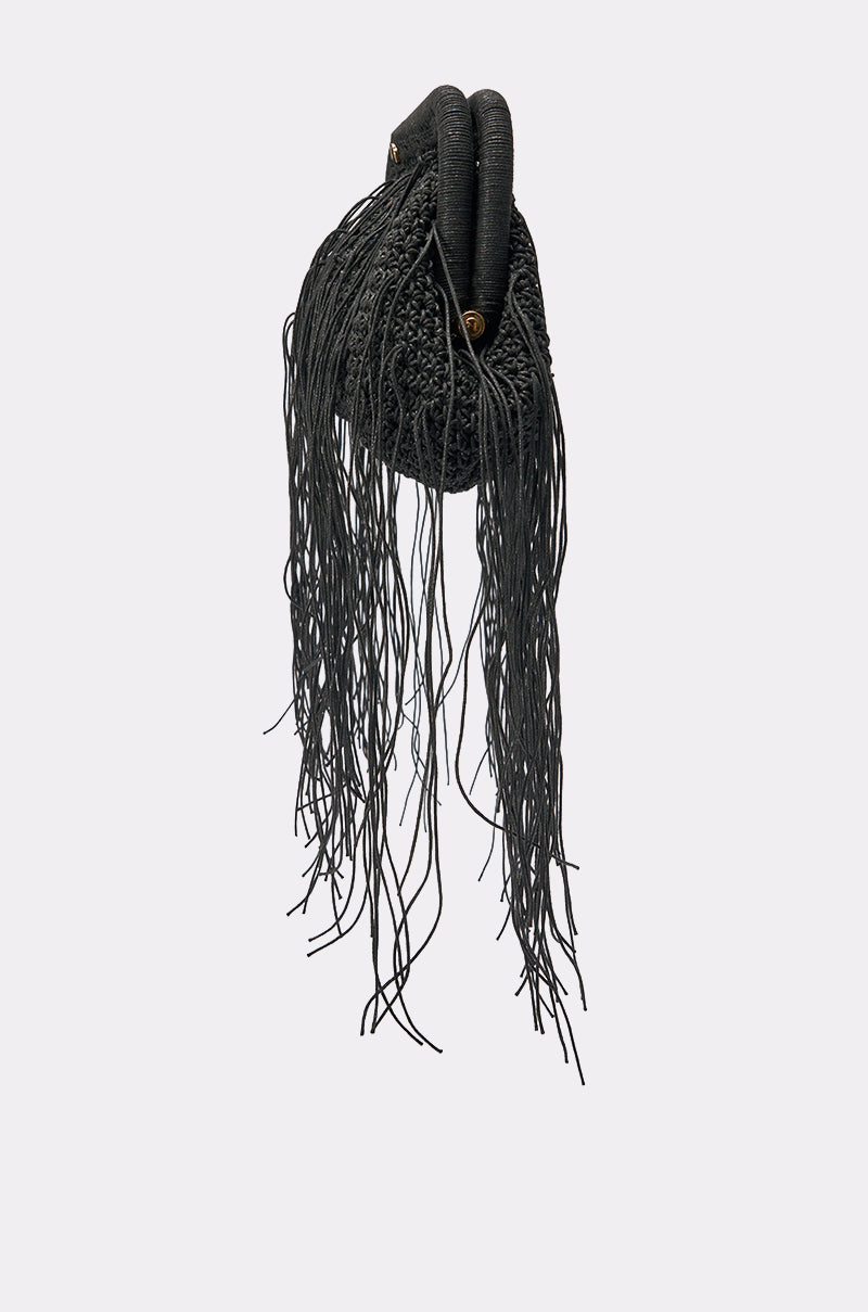 The IN THE WIND CLUTCH is a black statement purse with textured fabric, long thin fringe, two thick handles, and gold hardware—an eye-catching accessory for girls’ night out, shown against a plain light grey background. 2