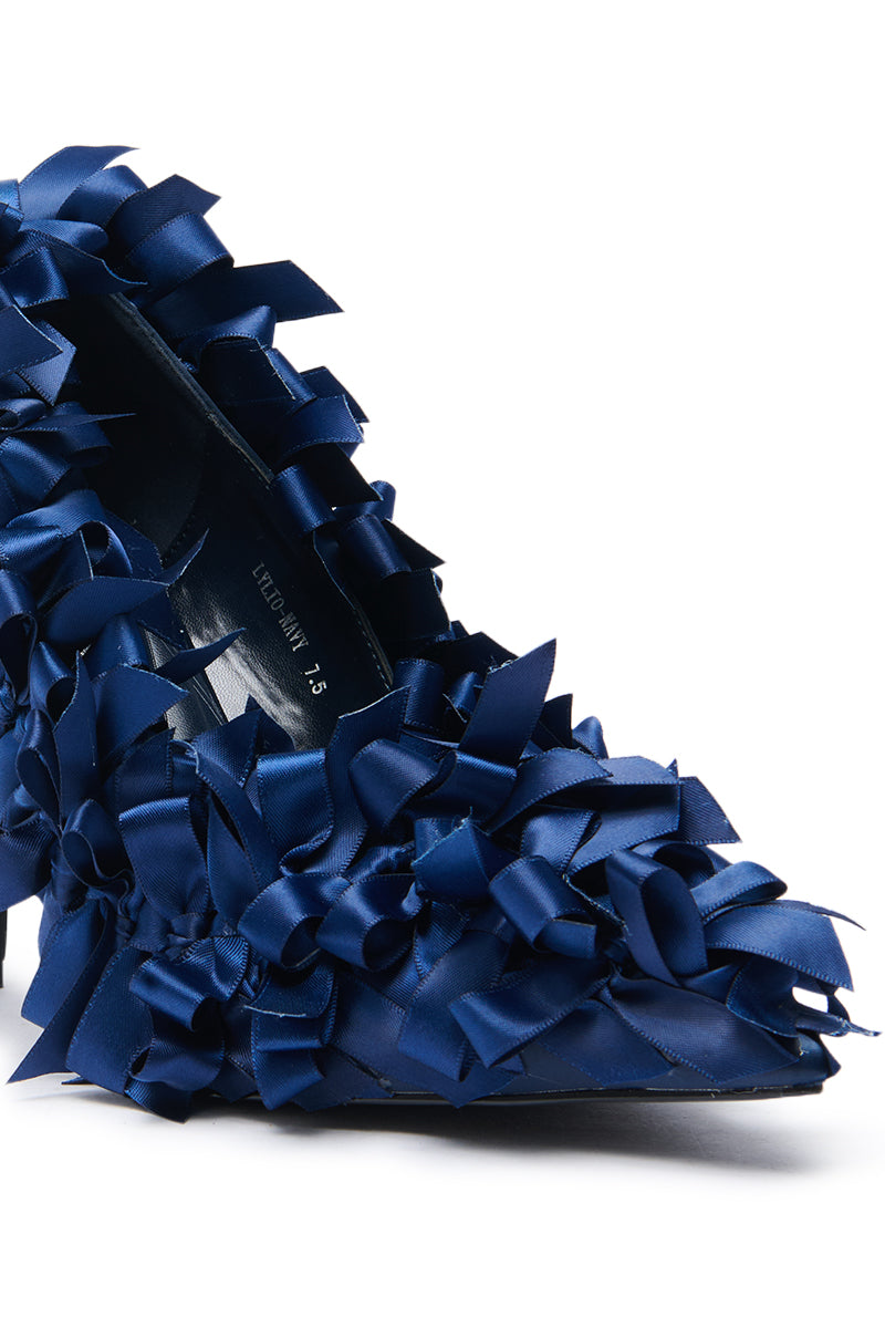 A close-up highlights the AZALEA WANG LYLIO NAVY BOW EMBELLISHED PUMP, featuring a pointed toe stiletto heel adorned with shiny dark blue satin bows for a richly textured, decorative look.