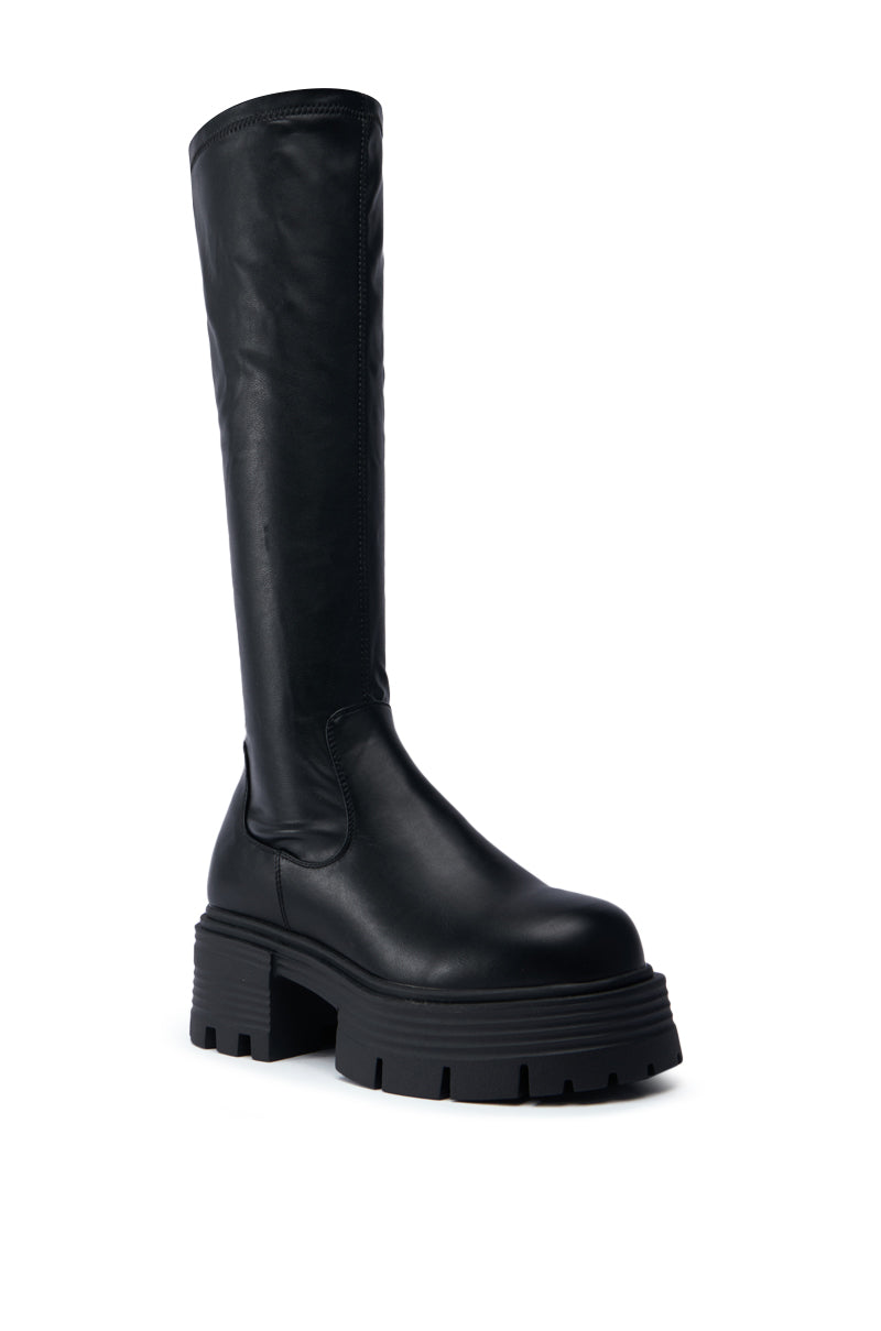 The SLIM FIT AZALEA WANG LYNX BOOT WITH 4 WAY STRETCH IN BLACK is showcased against a white backdrop, highlighting its black knee-high design with a chunky heel and smooth leather finish. This boot features a round toe and sturdy platform, melding modern aesthetics with its sleek knee-high shaft for a striking appearance.