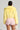 A person is seen from the back wearing the POPPY CROPPED FUR COAT IN YELLOW, featuring an oversized lapel collar, paired with pink lace shorts. Their hair is styled in a bun, and they hold a fluffy white purse against a simple light-colored background.