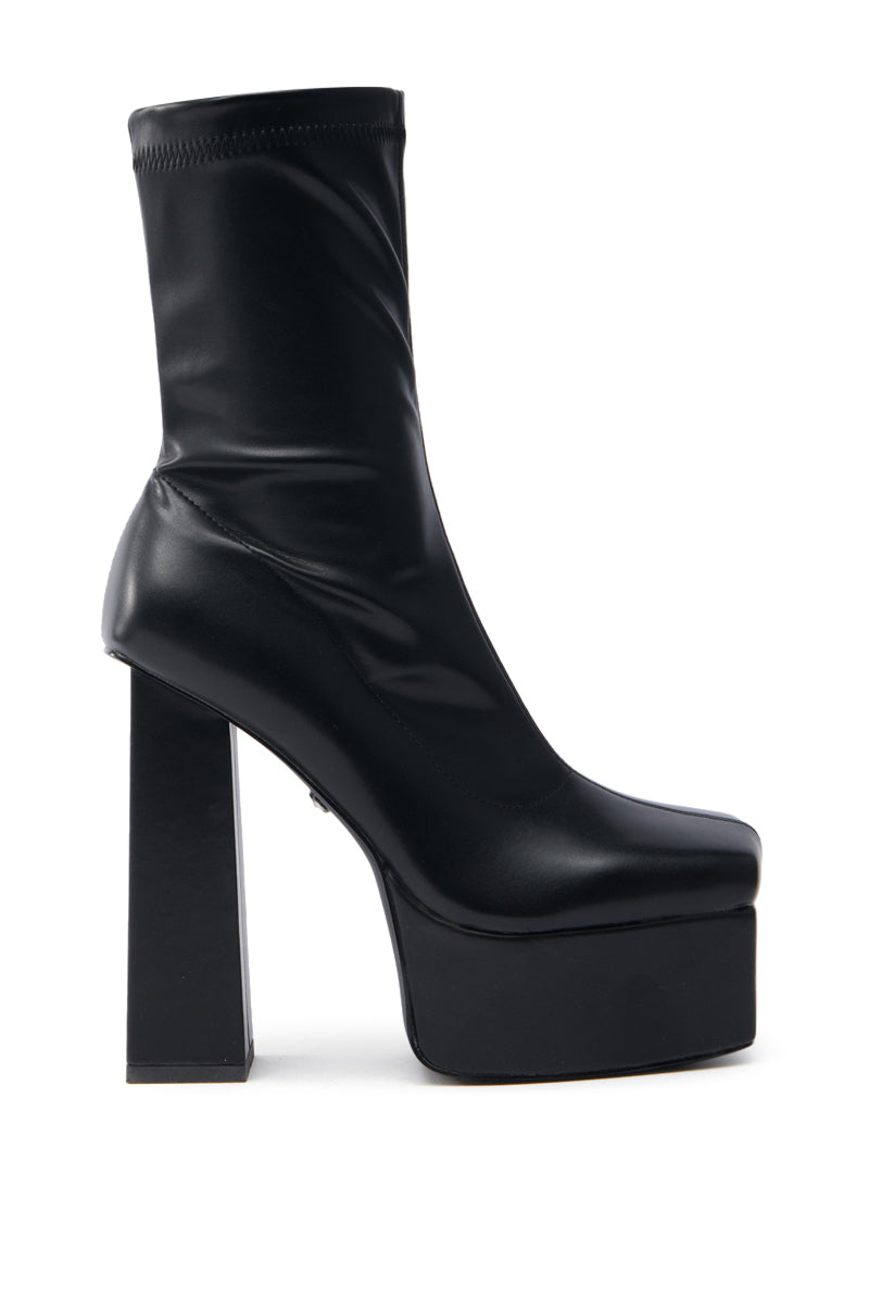 The AZALEA WANG MADDER BLACK PLATFORM BOOTIE is a sleek, ankle-length shiny black bootie with a chunky heel and thick platform sole. Crafted from smooth faux leather, it features a tall, square block heel.