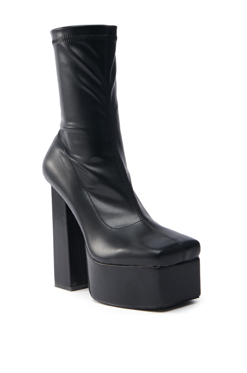The AZALEA WANG MADDER BLACK PLATFORM BOOTIE is a black shoe with a glossy faux leather finish, featuring a square toe and chunky block heel, showcased on a plain white background.