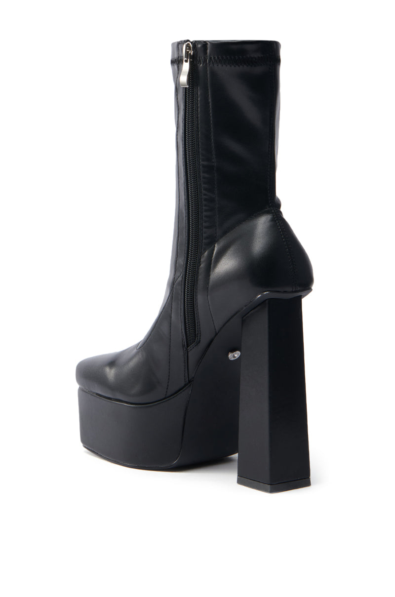 The AZALEA WANG MADDER BLACK PLATFORM BOOTIE is a black high-heeled bootie with a chunky heel, square block design, and a side zipper. It has a sleek, modern appeal with a glossy faux leather finish and an angled silhouette to highlight its stylish profile.