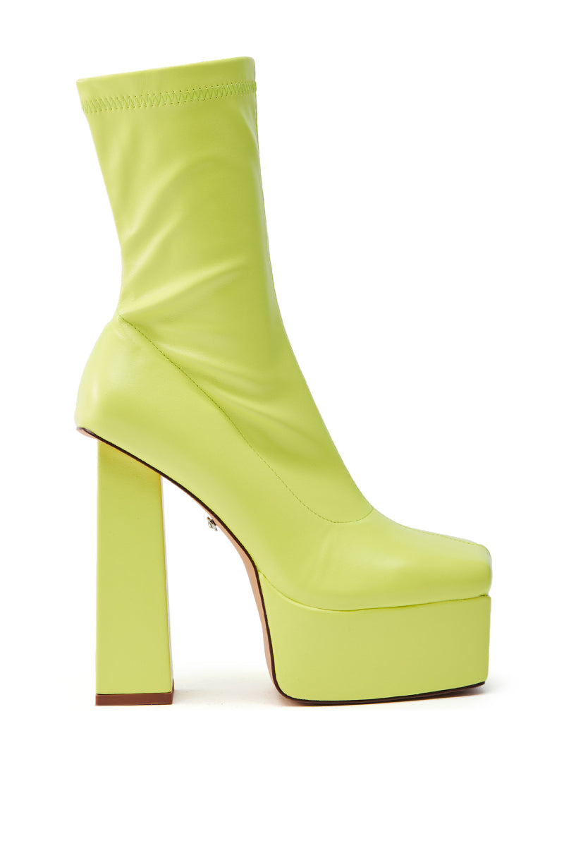 The AZALEA WANG MADDER LIME PLATFORM BOOTIE is a lime green, knee-high boot with a squared toe and chunky high heel. It's crafted from sleek faux leather with a platform sole and smooth finish, presented on a plain white background.