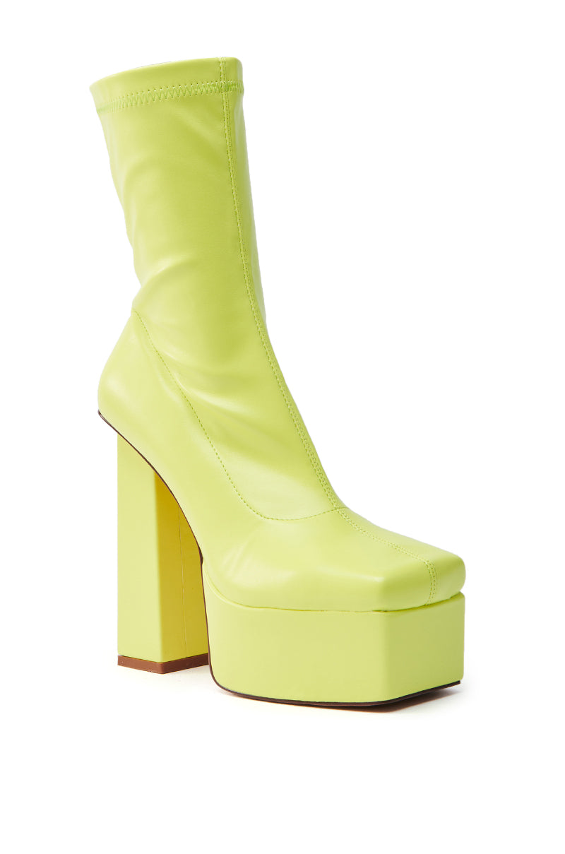 The AZALEA WANG MADDER LIME PLATFORM BOOTIE is a faux leather shoe in bright neon yellow. It features a chunky heel and thick sole, with a sleek, form-fitting upper that stands out against a crisp white background.