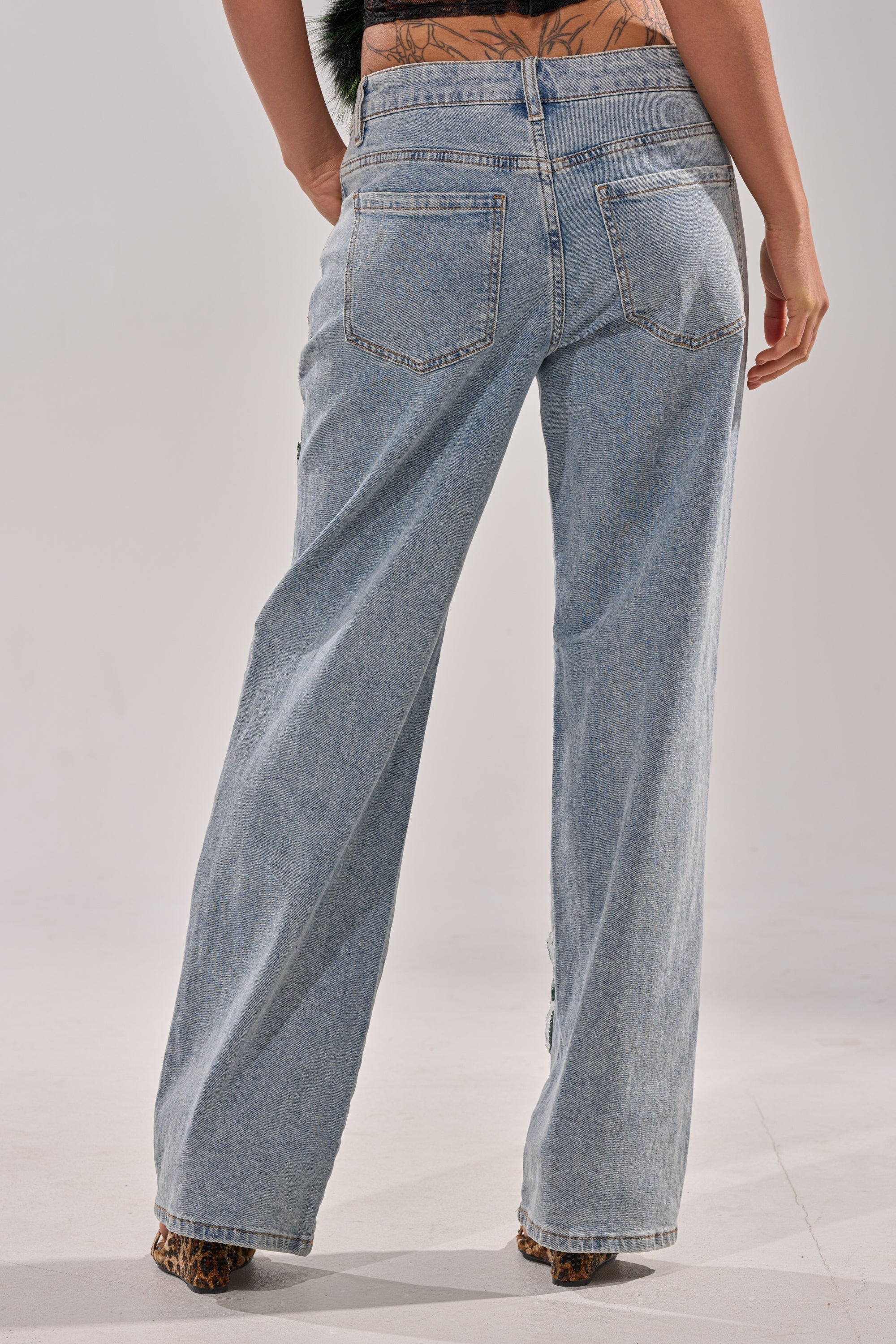 Someone wearing the BILLIONAIRE BELLE RHINESTONE JEANS, featuring a high-rise waist and light-wash denim. 4