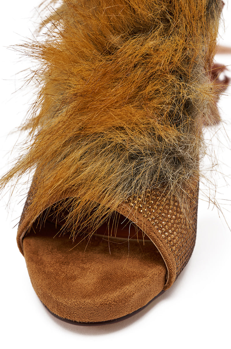 A close-up of the AZALEA WANG MADHAV Bronze Rhinestone and Fox Fur Sandal featuring a brown open-toe design with textured material and long, shaggy fox fur detailing on the upper.