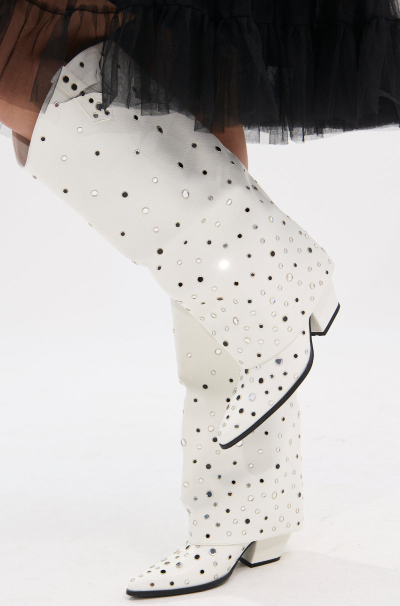A person in a black tulle skirt stands with one leg crossed, wearing the AZALEA WANG MADLOCK WHITE EMBELLISHED WESTERN BOOT featuring cutout details and black accents.